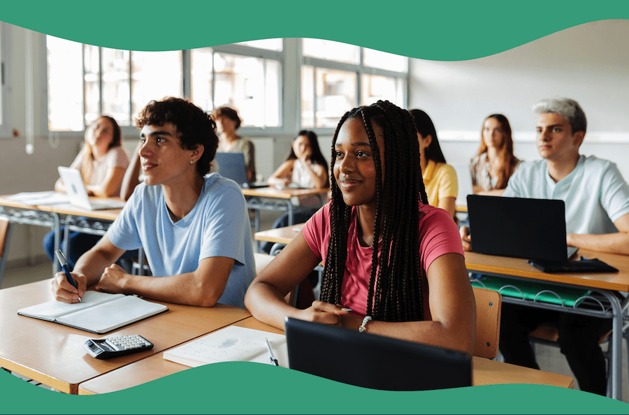 A group of students sit attentively in a sunny classroom. In the front, two students sit with a laptop, notebooks open and a calculator on the table.
