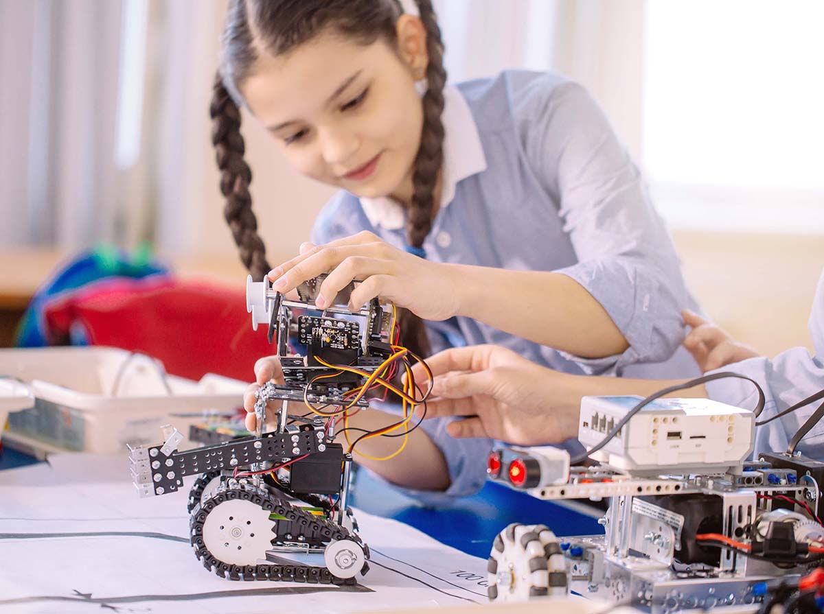 Concentrated smiling Caucasian girl creating technical toy at technical hobby club.