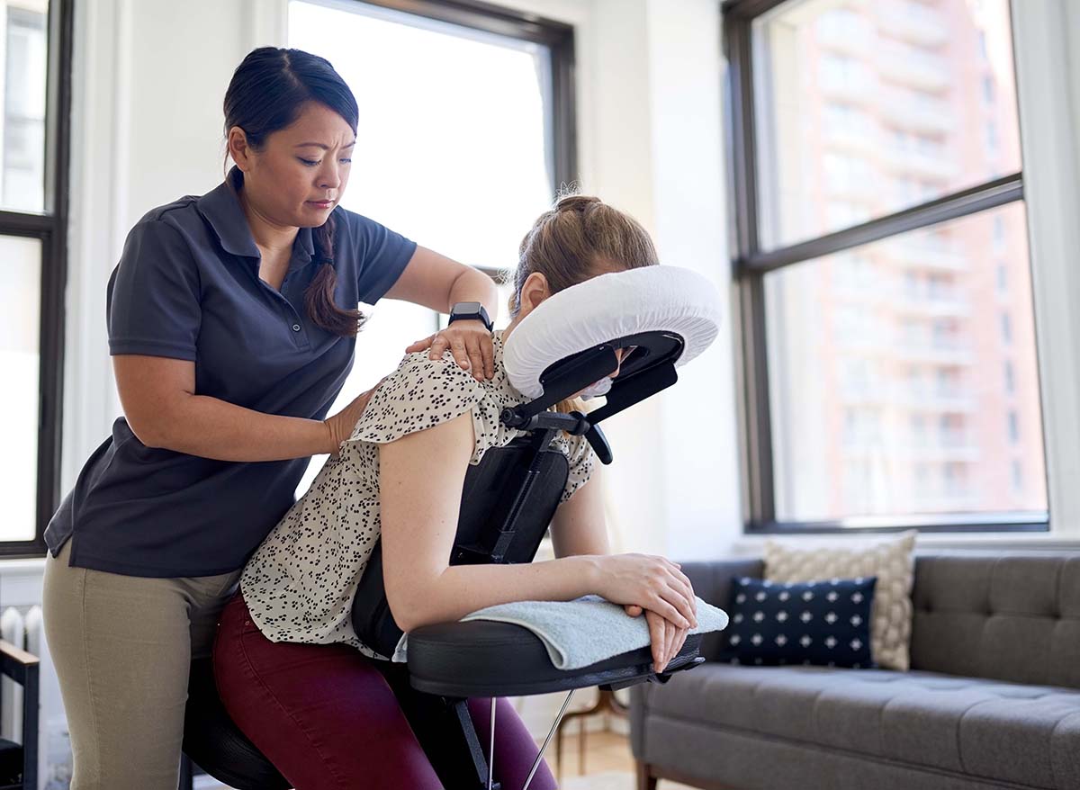 Candid image of an employee getting a chair massage during a appointment with a professional Asian physiotherapist in a kinesio clinic.